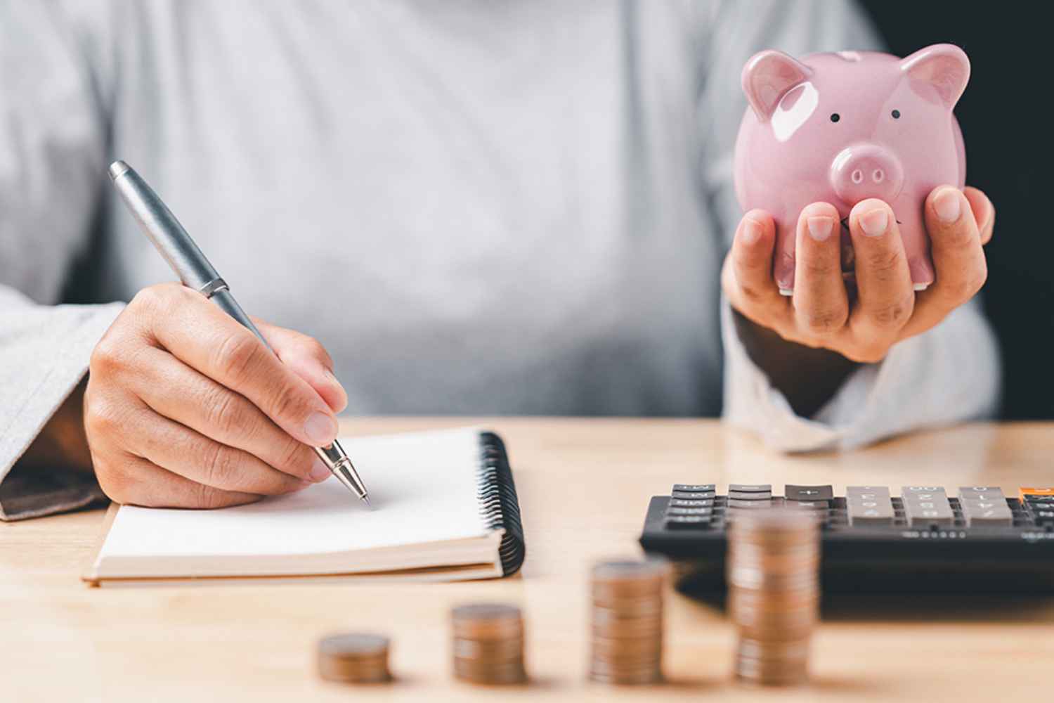 Hand mit Notizbuch und Sparschwein
