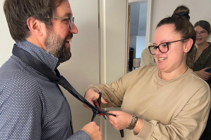 Mitarbeiterin schneidet einem Mitarbeiter die Krawatte